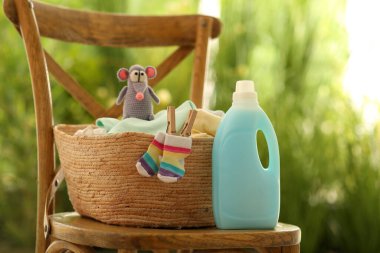 Bir şişe deterjan ve çocuk giysileri dışarıda sandalyede.