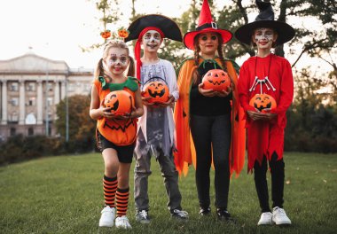 Cute little kids with pumpkin candy buckets wearing Halloween costumes in park clipart
