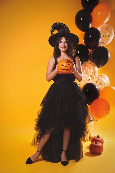 Gyönyörű Boszorkányjelmezben Lufikkal Tök Sárga Háttérrel Halloween Buli — Stock Fotó