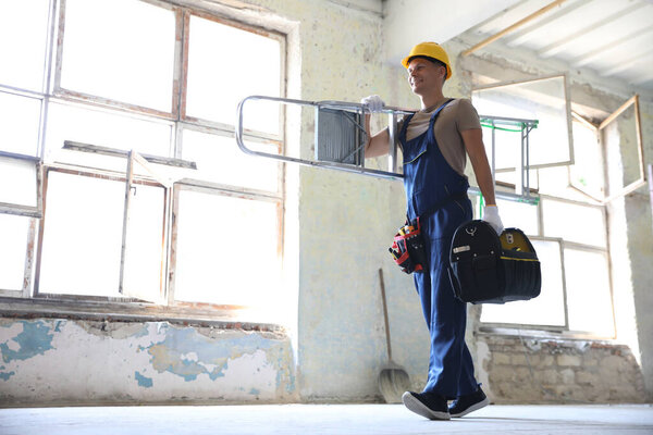 Professional constructor with ladder and toolbox in old building