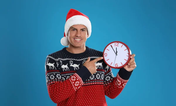 サンタの帽子の男は青い背景に時計をつけている クリスマスカウントダウン — ストック写真