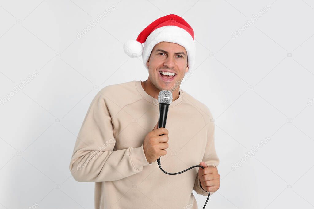 Happy man in Santa Claus hat singing with microphone on white background. Christmas music