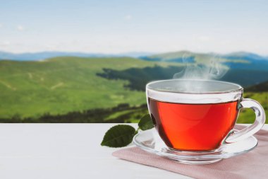 Ahşap masada, bulanık dağ manzarasına karşı cam bardak sıcak çay. Metin için boşluk