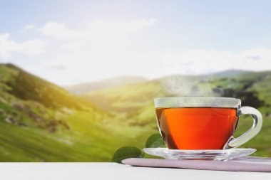 Ahşap masada, bulanık dağ manzarasına karşı cam bardak sıcak çay. Metin için boşluk