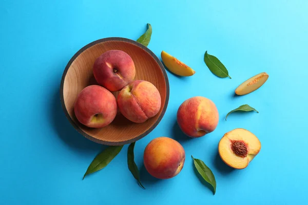 Fresh ripe peaches and green leaves on light blue background, flat lay