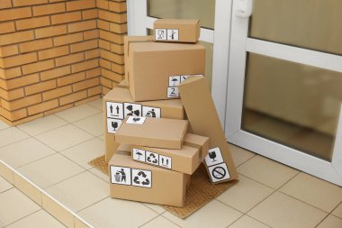 Giriş kapısının yanındaki paspasın üzerinde farklı ambalaj sembolleri olan karton kutular. Paket teslimi