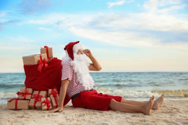 Noel Baba bir çanta dolusu hediyeyle kumsalda dinleniyor, mesaj için yer açıyor. Noel tatili