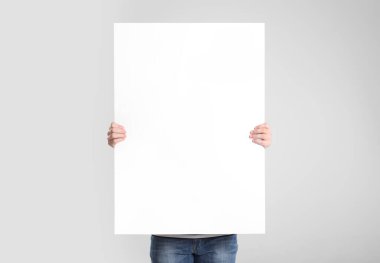 Açık gri arkaplanda boş poster tutan adam