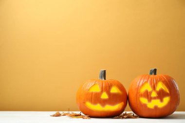 Korkunç Jack O 'Lantern balkabakları ve beyaz ahşap masa üzerindeki yapraklar sarı arka planda, mesaj için yer var. Cadılar Bayramı Dekorasyonu