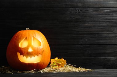 Balkabağı Jack O 'Lantern, saman ve sonbahar yaprakları siyah ahşap masada, yazı için yer var. Cadılar Bayramı Dekorasyonu