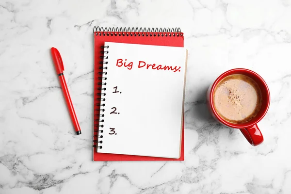 Notebook with dreams list on white marble table, flat lay