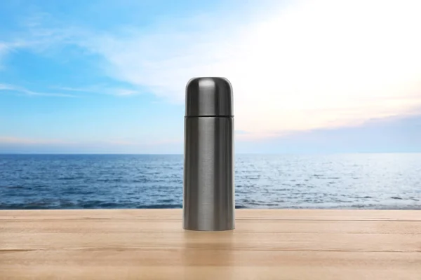蓝色天空下靠近大海的木制桌子上的热水瓶 — 图库照片