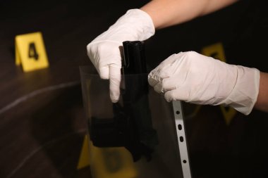 Dedektif olay yerinde plastik torbaya silah koydu, yakın plan.