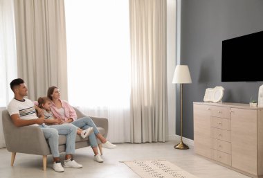 Mutlu bir aile evdeki kanepede televizyon izliyor.