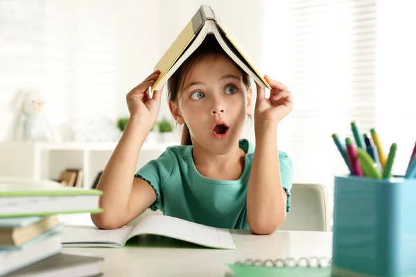 Emocional Niña Con Libro Cabeza Haciendo Tarea Mesa Interior — Foto de Stock