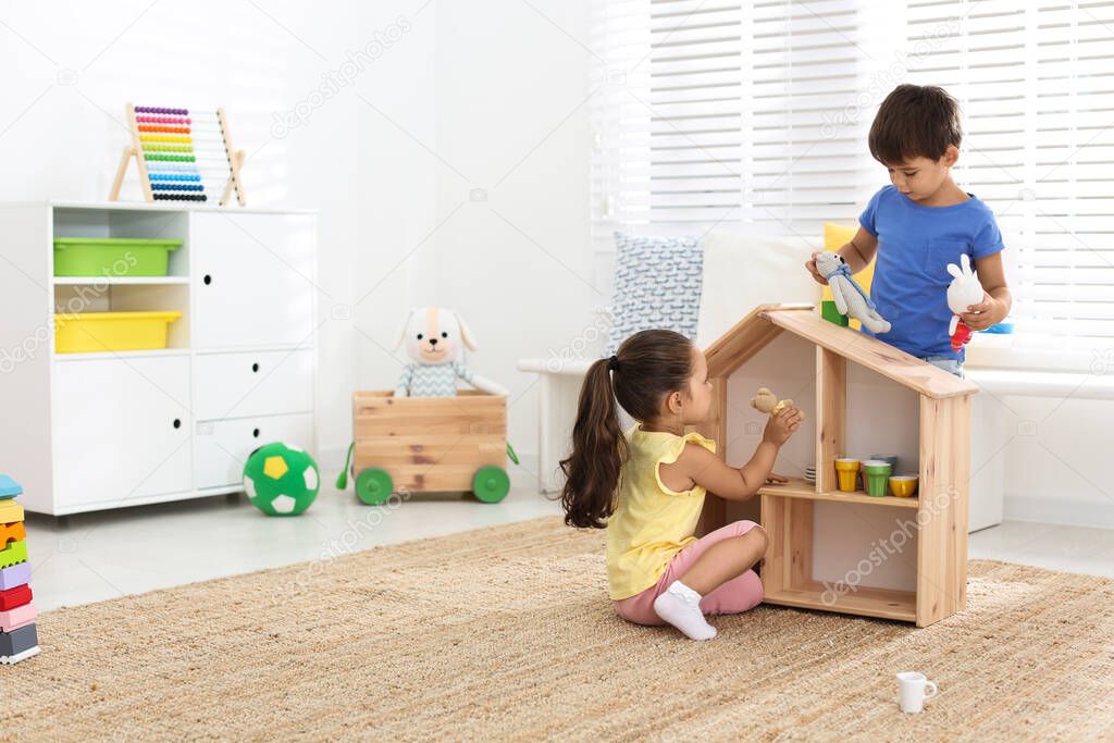 Cute little children playing with toys near wooden house on floor at home, space for text