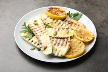 Lezzetli ızgara kabak dilimleri, balkabağı tohumları, limon ve maydanoz gri masada, yakın plan.