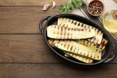 Lezzetli ızgara kabak dilimleri fırın kabında, yağ ve baharatlar ahşap masada, düz bir şekilde. Metin için boşluk