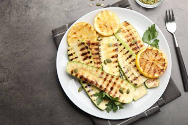 Gri desenli masada servis edilen balkabağı tohumlu, limonlu ve maydanozlu lezzetli ızgara kabak dilimleri. Metin için boşluk