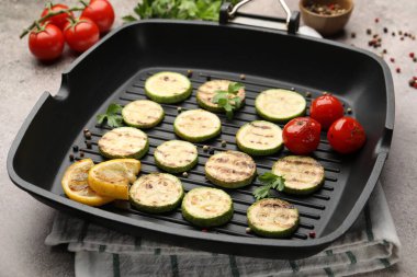 Lezzetli ızgara kabak dilimleri domatesli, limonlu ve maydanozlu tavada gri desenli masa, yakın plan.