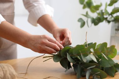 Çiçekçinin ahşap masasında okaliptüs dallarından güzel bir buket yapıyor.