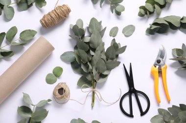 Çiçekçi. Beyaz masa üzerinde okaliptüs dalları, iplikler, makas, budama ve ambalaj kağıdı düz.