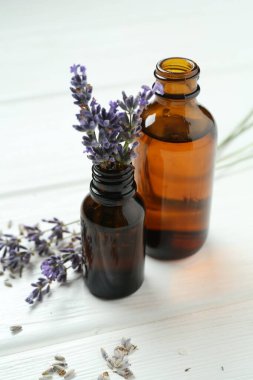 Lavanta yağı ve çiçekler beyaz ahşap masada, yakın plan.