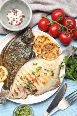 Açık mavi ahşap masada servis edilen limon dilimli ve otlu kızarmış balık. Ev yapımı deniz ürünleri yemeği.