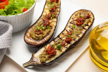 Izgara patlıcan dilimleri, güneşte kurutulmuş domates, pesto ve salata, yakın plan.