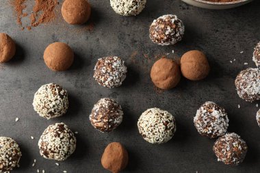 Kakao tozu, fındık, hindistan cevizi gevreği ve susam tohumlu lezzetli çikolata şekerleri gri masada, düz yerde.