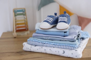 İçerideki ahşap masada temiz bebek kıyafetleri ve ayakkabılar yığını.