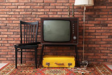 Retro TV, bavul, lamba ve kırmızı tuğla duvarın yanında siyah sandalye. Kullanılmış eşyalar