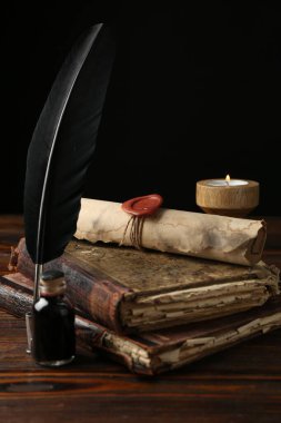 Eski parşömen, yanan mum, tüy, mürekkep hokkası ve ahşap masa üzerindeki kitaplar.