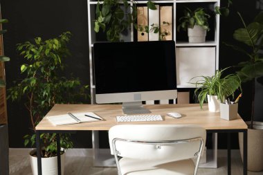 Modern bilgisayarı, kırtasiyesi ve çiçek dekoru olan şık bir iş yeri. Biyofilik iç tasarım