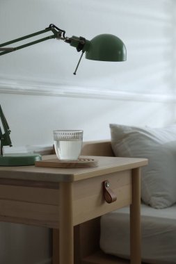 Yatak odasının yanında lamba ve bir bardak su olan komodin, yakın çekim.