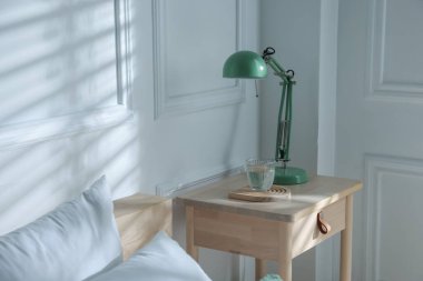 Yatak odasının yanında lamba ve bir bardak su olan komodinin yanında.