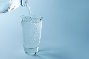 Açık mavi gradyan arka planda şişeden cama taze soda dökülüyor, yakın plan. Metin için boşluk