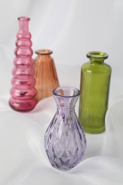 Beyaz kumaş üzerinde farklı güzel cam vazolar, yakın plan.