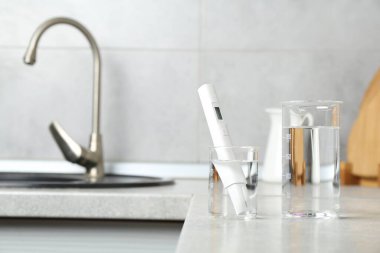 Mutfakta lavabonun yanında temiz su ve dijital pH ölçer bulunan deney şişeleri, yakın plan. Metin için boşluk