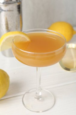 Bardakta limon dilimli martini kokteyli, beyaz ahşap masada meyve ve karıştırıcı, yakın plan.