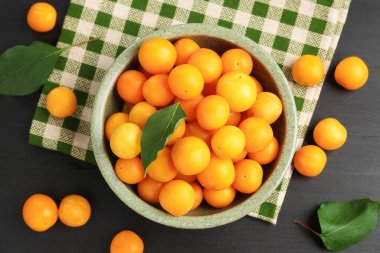 Olgun sarı kiraz erikleri, siyah ahşap masa üzerinde yapraklar, düz yatıyordu.