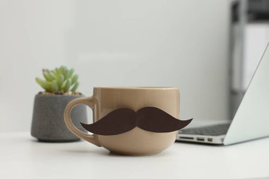 Babalar Günün kutlu olsun. Kağıt bıyıklı kupa ve dizüstü bilgisayar kapalı beyaz masada, yakın plan.