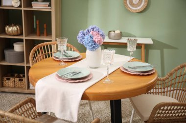 Yemek odasındaki ahşap masada, tabak ve vazo çiçekli şık bir ortam. İç tasarım