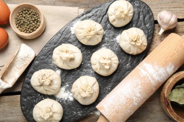 Pişmemiş khinkaliler (hamur köfteleri), un, baharatlar, yumurtalar ve tahta masanın üzerinde merdane.