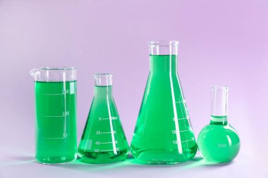 Eflatun arkaplanda yeşil sıvı bulunan laboratuvar camları.