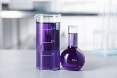 İçerideki ışık masasının üzerinde mor sıvı bulunan laboratuvar camları.