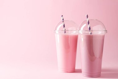 Pembe arka planda plastik bardaklarda lezzetli milkshake 'ler, metin için boşluk
