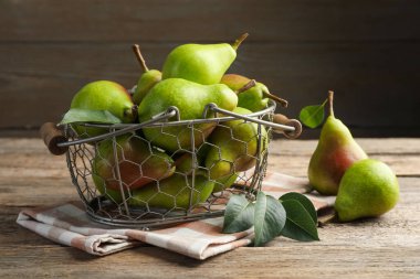 Metal sepetin içinde taze armutlar ve ahşap masada yeşil yapraklar