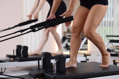 Kadın ve pilates eğitmeni stüdyoda reformcular üzerinde egzersiz yapıyor.