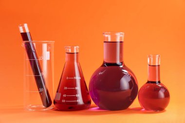Turuncu zemin üzerinde kırmızı sıvı bulunan laboratuvar camları.